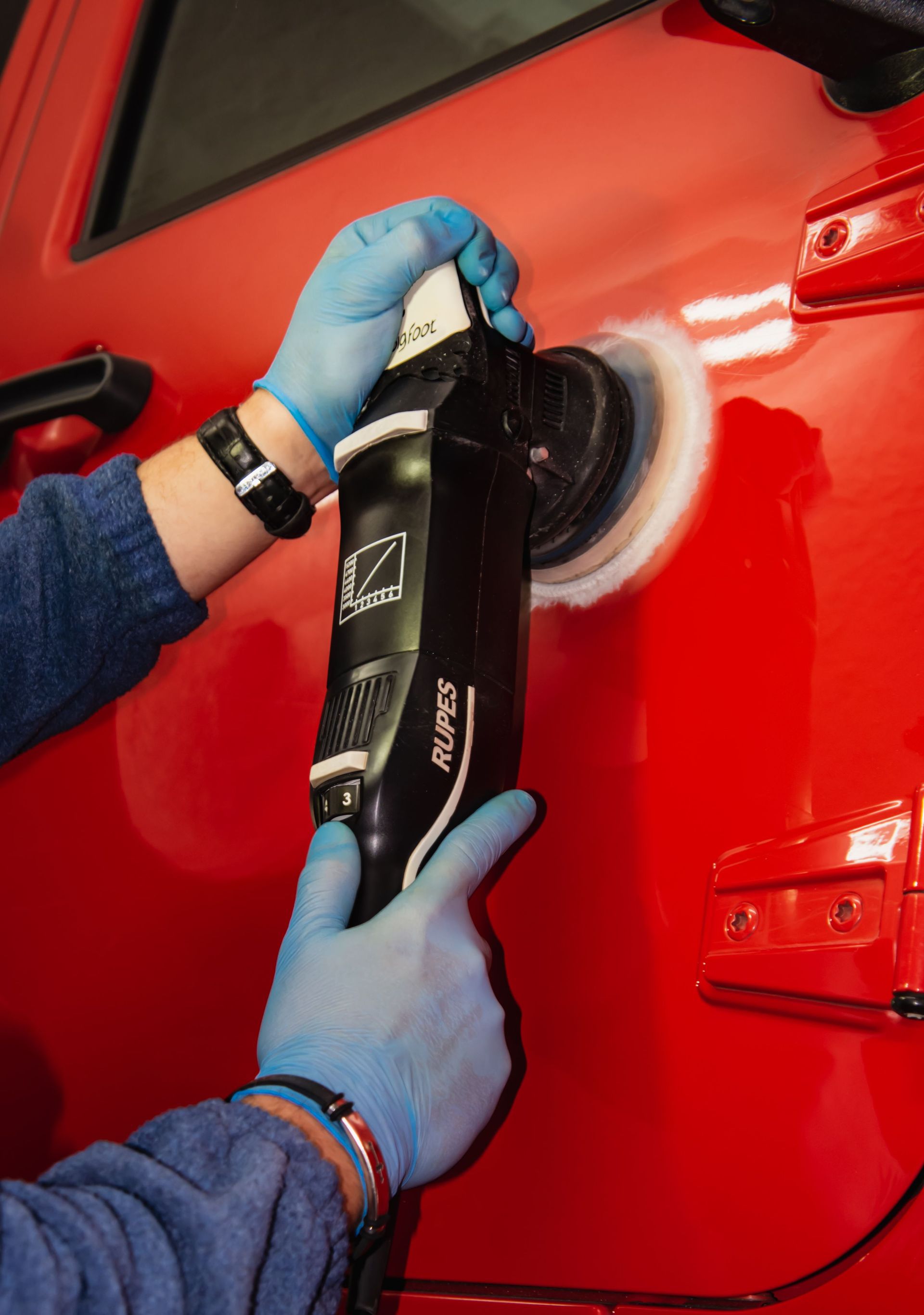 Detailed view of a car polishing tool in use on a vibrant red vehicle body.